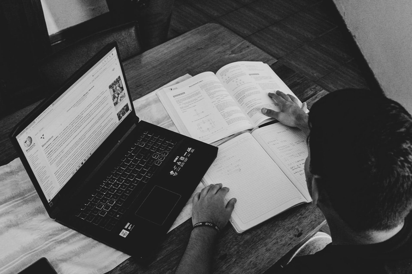 Student uczący się przy drewnianym biurku z laptopem i podręcznikiem.