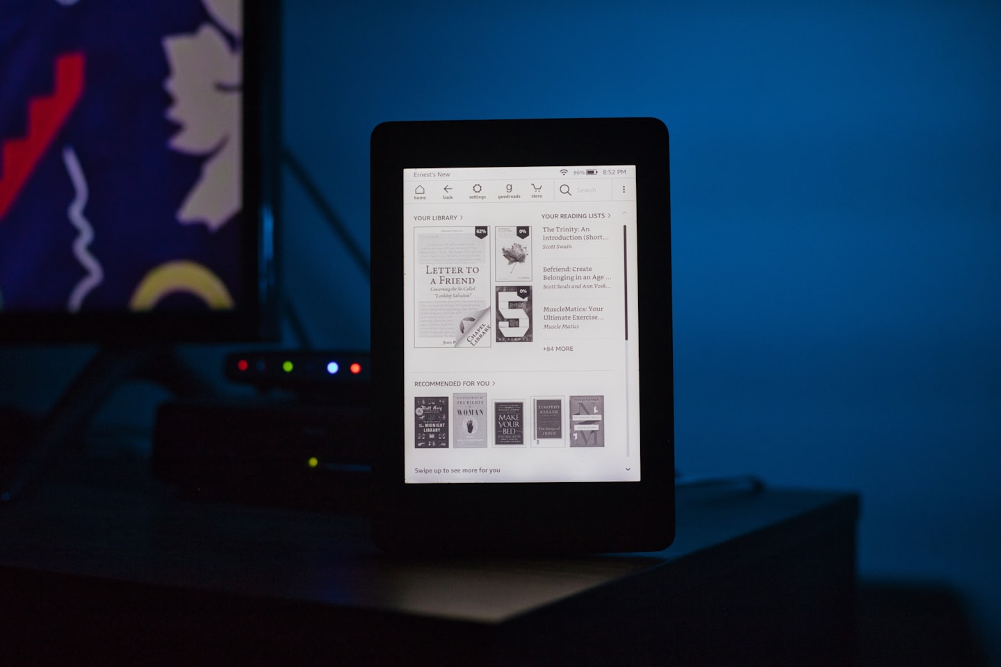 Czarny czytnik e-booków z okładkami książek na ciemnym drewnie.